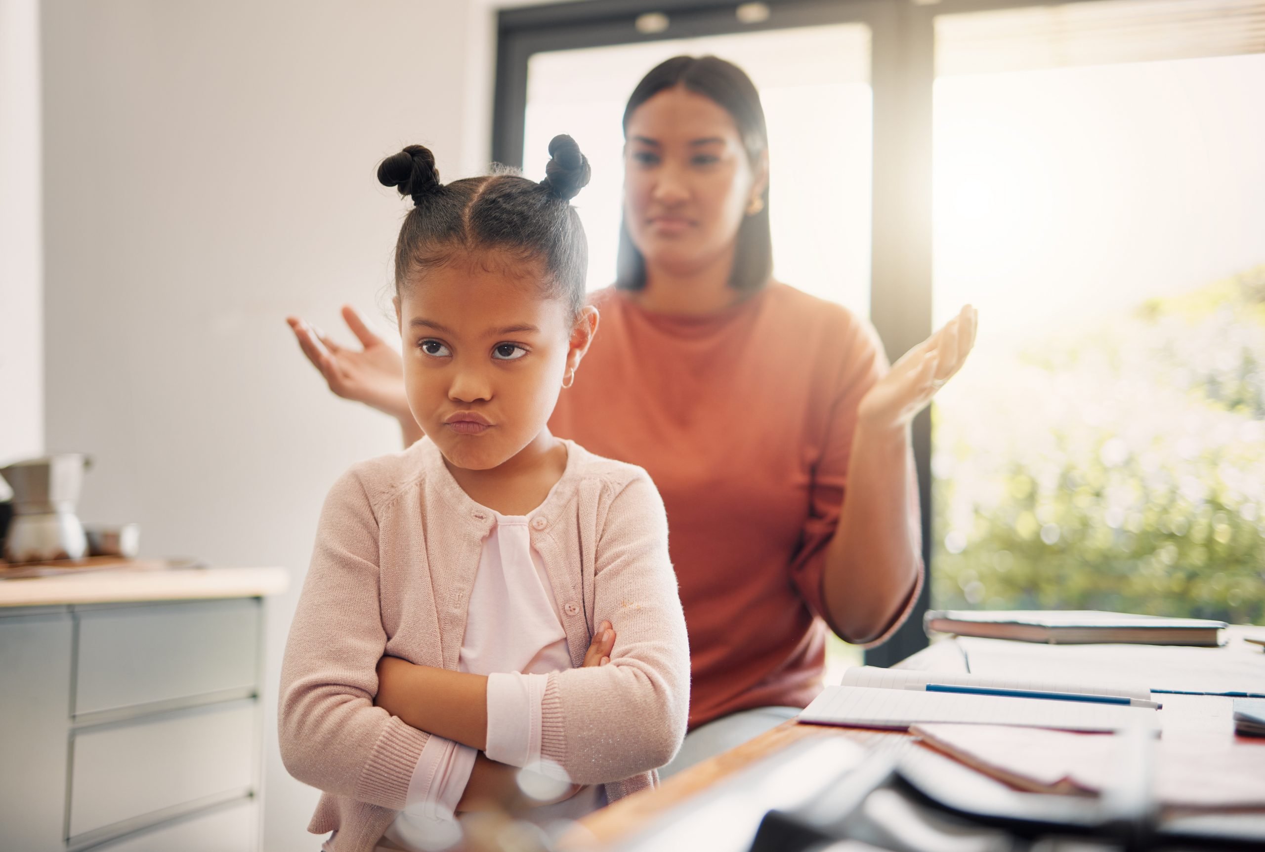 Upset, discipline and family while offended and stubborn little girl looking unhappy with her scolding mother in the background. Naughty, problem and bad child angry and ignoring her parent at home